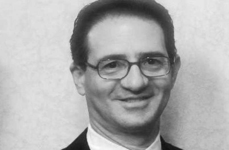 A black and white closeup headshot of a smiling man wearing glasses.